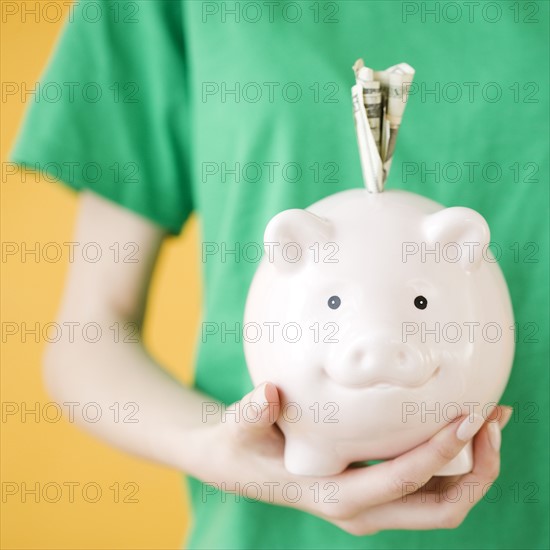 Woman holding piggy bank with money in slot. Date : 2008