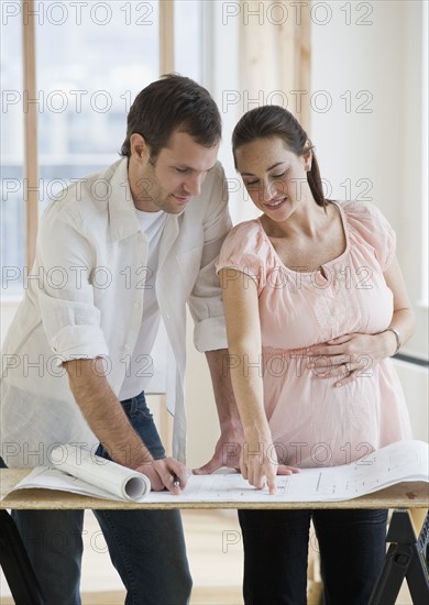 Pregnant Hispanic couple looking at blueprints.