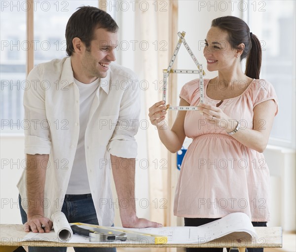 Pregnant Hispanic couple looking at ruler shaped like house.