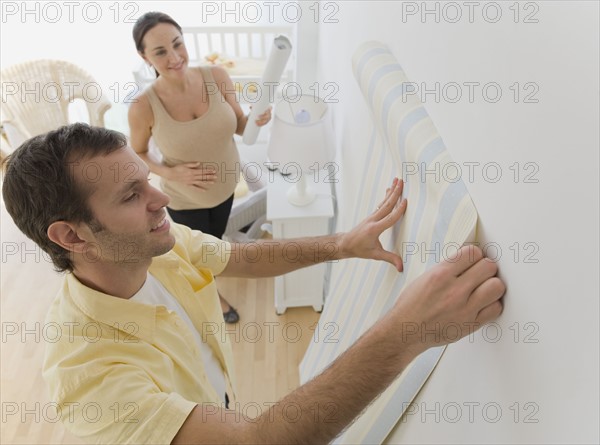 Pregnant Hispanic couple hanging wall paper in nursery.