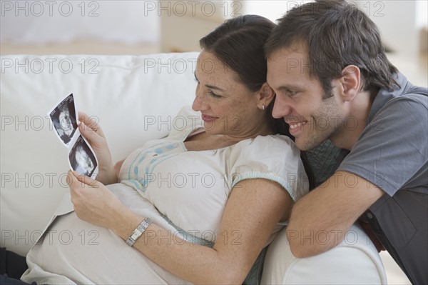 Pregnant Hispanic couple looking at ultrasound printout.