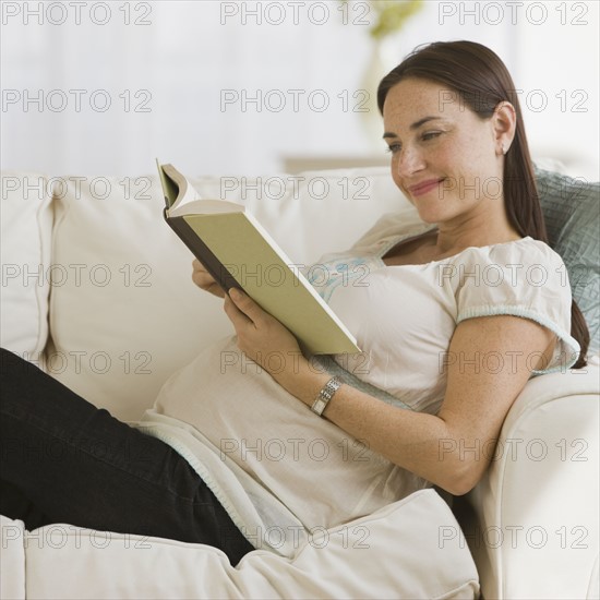 Pregnant Hispanic woman reading book.