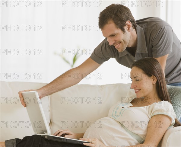 Pregnant Hispanic couple looking at laptop.