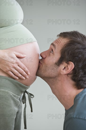 Hispanic man kissing pregnant wife’s belly.