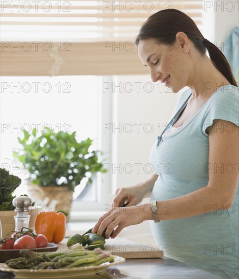 Pregnant Hispanic woman chopping vegetables.