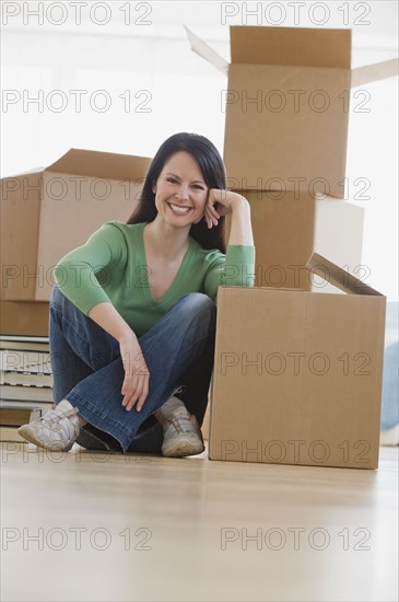 Woman leaning on moving box in new house.