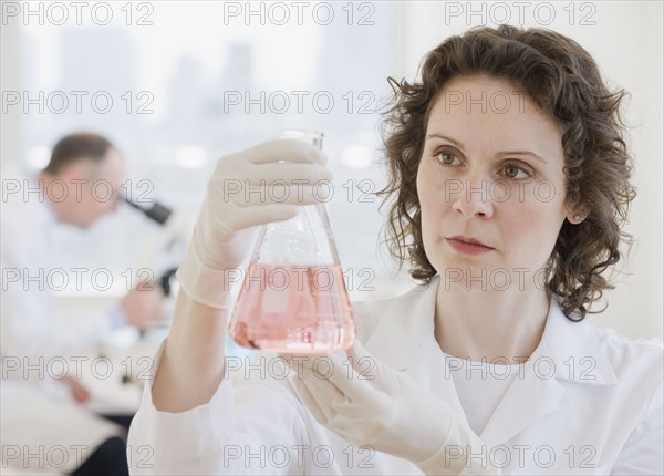 Female scientist looking at beaker of liquid.