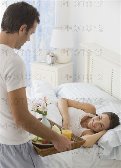 Hispanic man bringing wife breakfast in bed.