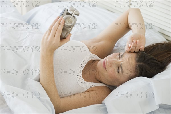 Hispanic woman looking at alarm clock.