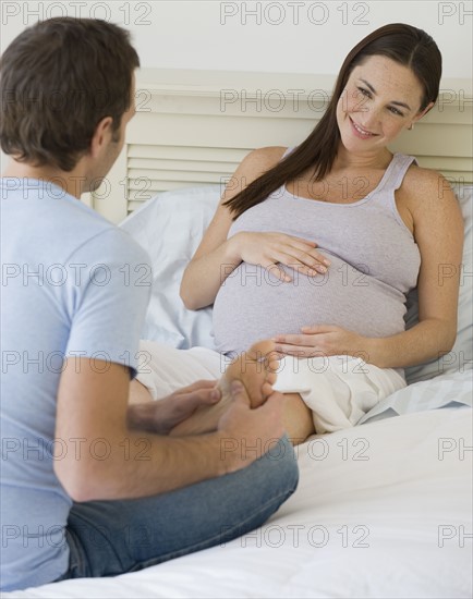 Hispanic man massaging pregnant wife’s foot.