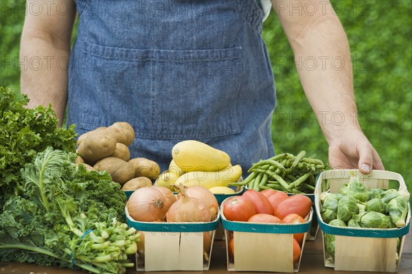 Farmer next to baskets of vegetables.