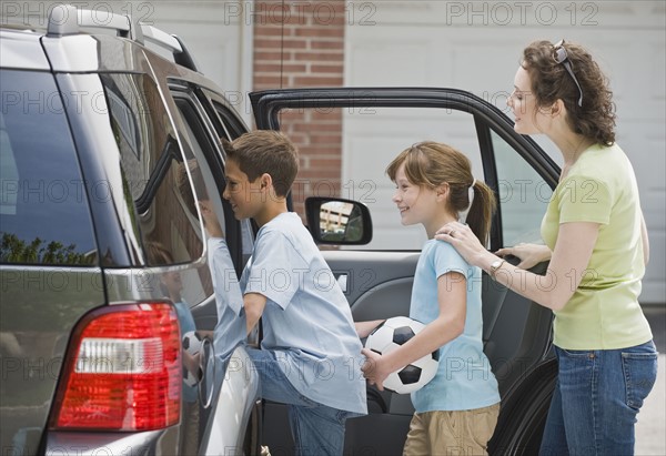 Mother and children getting into car with soccer ball.