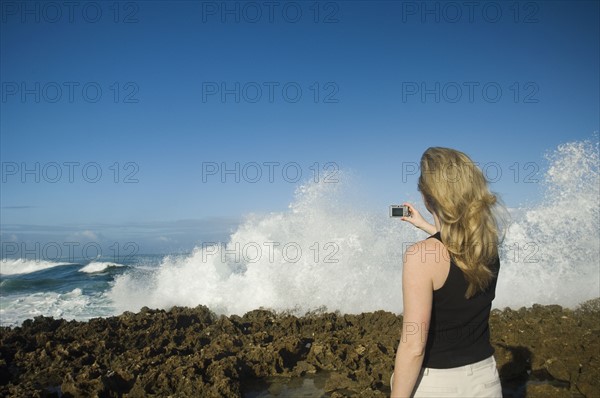 Woman taking photograph of ocean, Oahu, Hawaii, United States. Date : 2008
