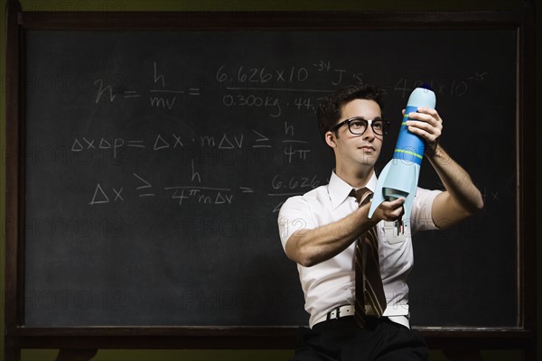 Nerdy man holding rocket model in front of blackboard. Date : 2008