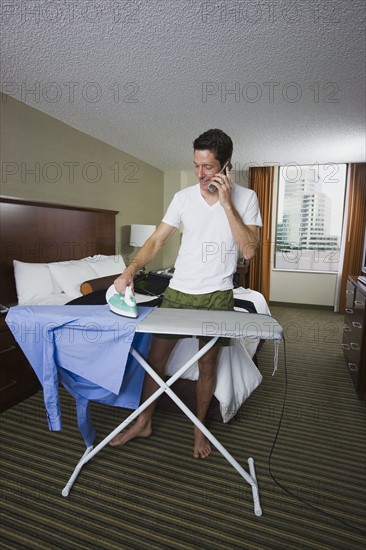Businessman ironing shirt and talking on cell phone. Date : 2008