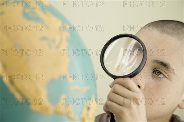 Boy examining globe with magnifying glass. Date : 2008