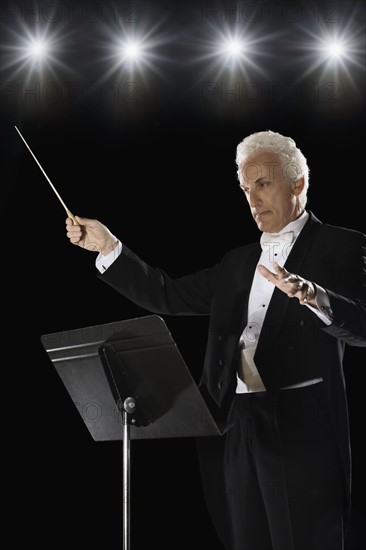 Man in tuxedo conducting under lights. Date : 2008