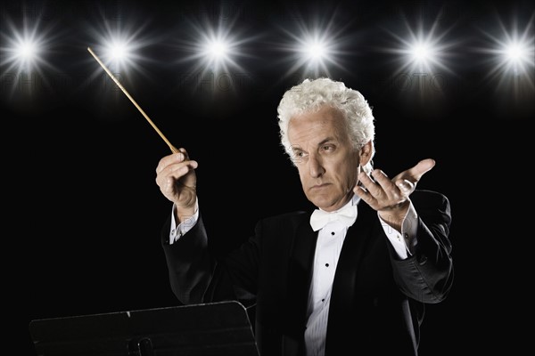 Man in tuxedo conducting under lights. Date : 2008