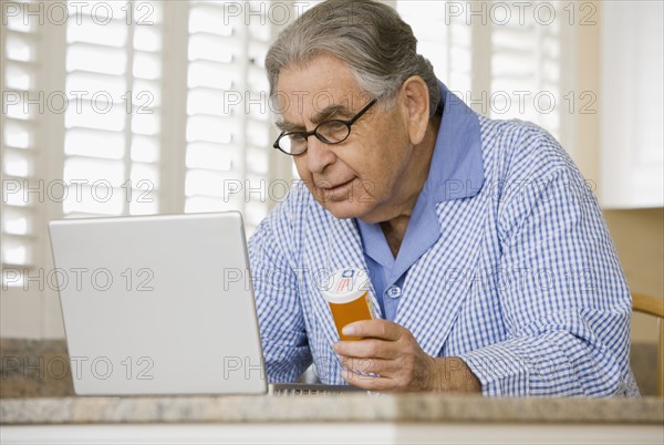 Senior man with medication bottle looking at laptop. Date : 2008