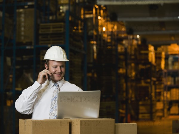 Businessman talking on cell phone in warehouse. Date : 2008