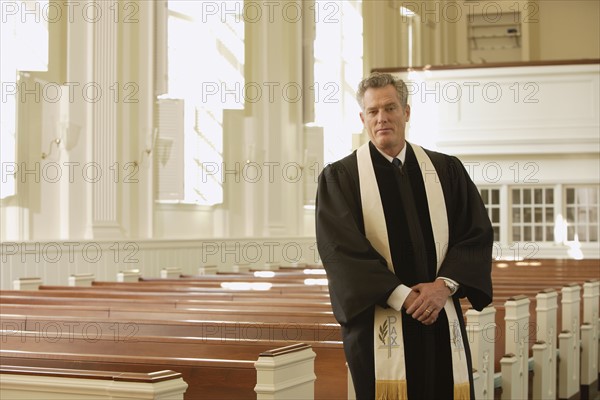 Priest standing next to pews. Date : 2008