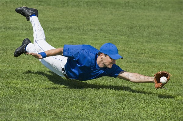 Baseball player diving to catch baseball.