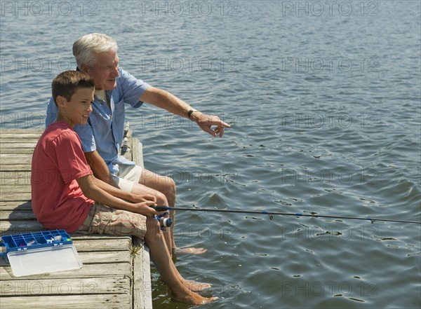 Grandfather and grandson fishing off dock.