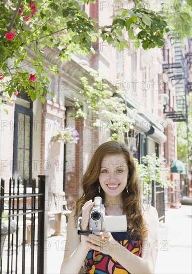 Woman holding video camera in urban setting. Date : 2008