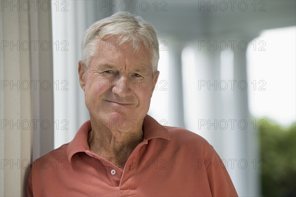 Senior man leaning against column.