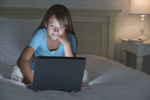Girl using laptop on bed.