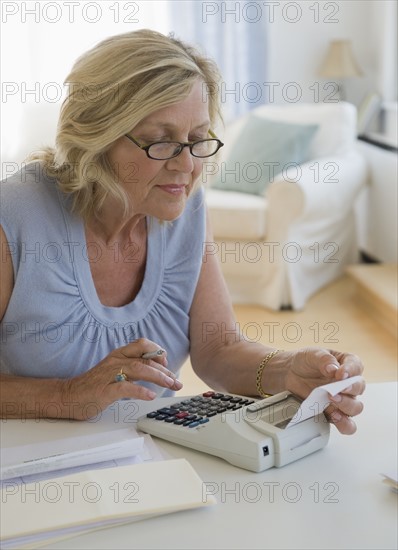 Woman using adding machine at home.