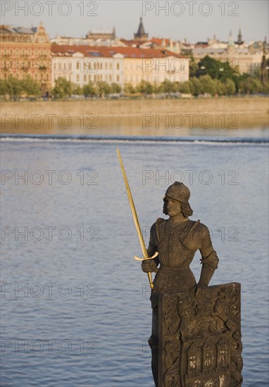 Statue in front of river and city.