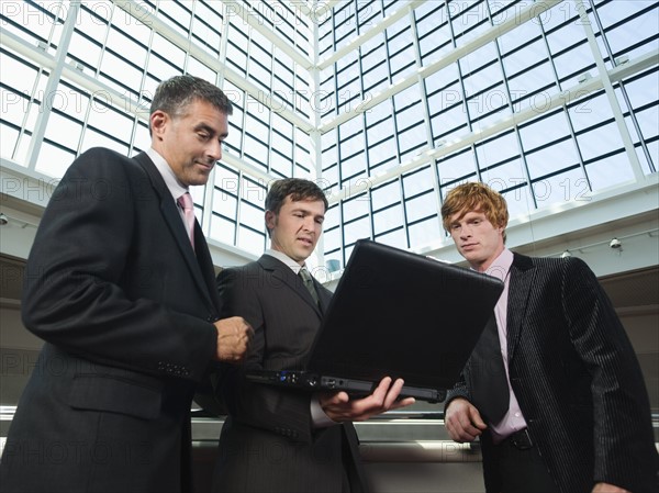 Businessmen looking at laptop in convention center atrium. Date : 2008