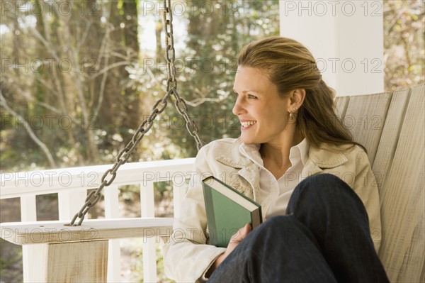 Woman relaxing with book on porch swing. Date : 2008