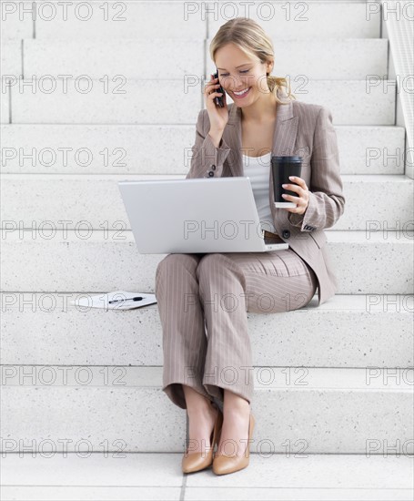 Businesswoman working on laptop and talking on cell phone. Date : 2008