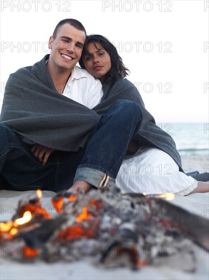 Young couple relaxing by campfire on beach. Date : 2008