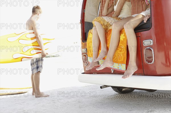 Young surfers relaxing by van on beach. Date : 2008