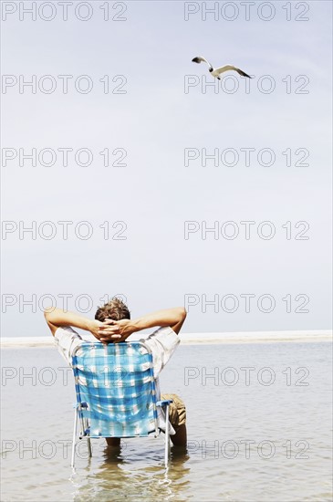 Man relaxing in lounge chair in middle of water. Date : 2008