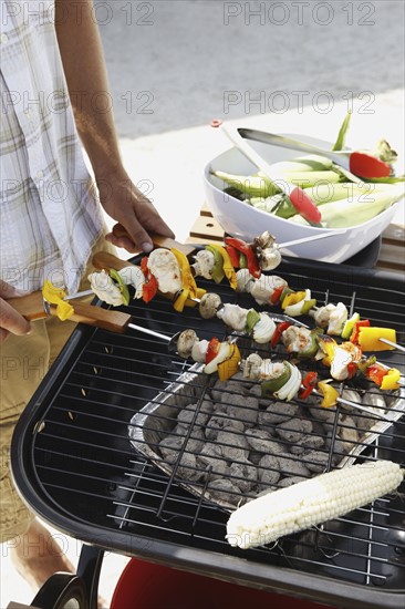 Man grilling shish kebabs and corn. Date : 2008