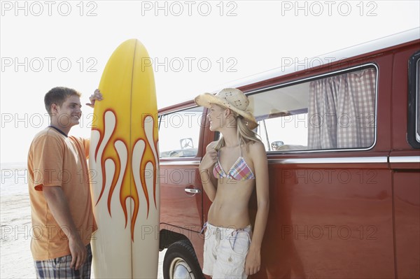 Young couple standing with surfboard by van on beach. Date : 2008