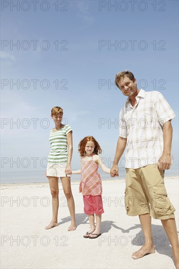 Girl holding hands with mother and father on beach. Date : 2008