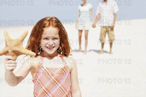 Girl holding up starfish on beach. Date : 2008