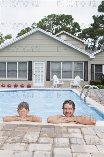 Father and son leaning on edge of swimming pool. Date : 2008