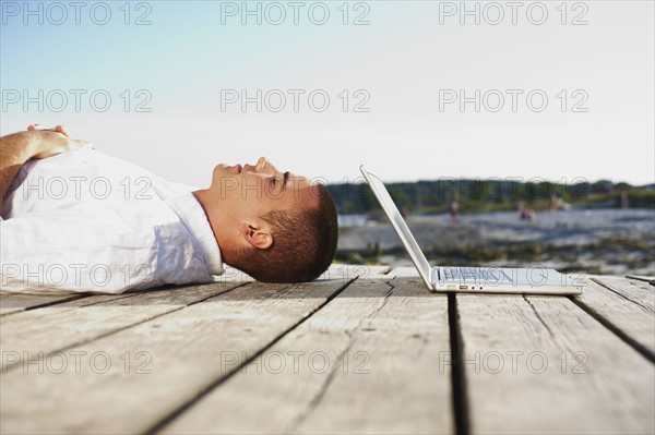 Man sleeping next to laptop on dock. Date : 2008