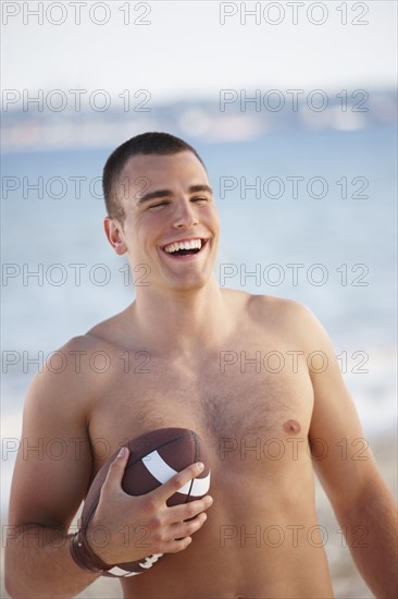 Young man holding football on beach. Date : 2008