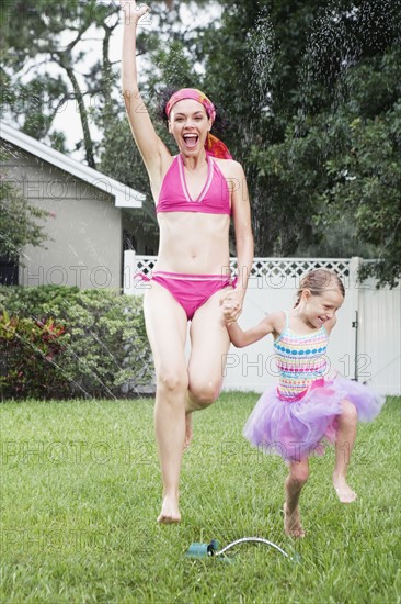 Mother and daughter running through sprinkler. Date : 2008