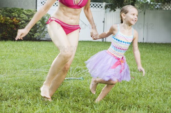 Mother and daughter running through sprinkler. Date : 2008