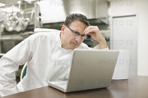 Frustrated chef looking at laptop in kitchen. Date : 2008