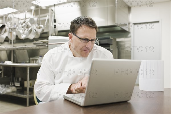 Frustrated chef looking at laptop in kitchen. Date : 2008
