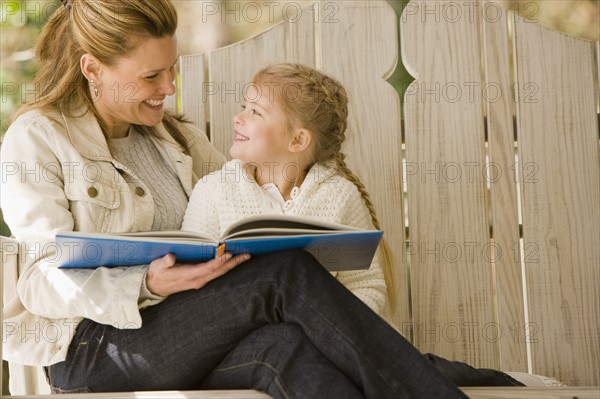 Mother reading to daughter on porch swing. Date : 2008